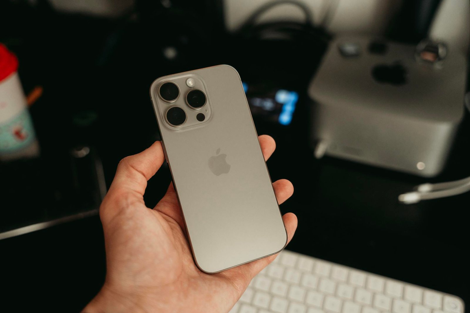 A hand holding a sleek smartphone in a tech-savvy office environment, showcasing its design.